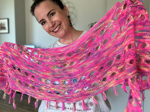 woman is holding up a hot pink knit shawl with openwork stitches and fringe