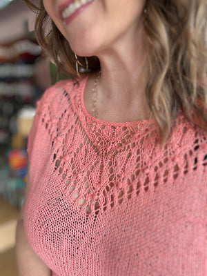 closeup image of the knit fabric of a summery lacy tee modeled on a woman