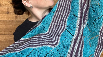 a woman is displaying a large triangle handknit shawl with alternating stripes and lace