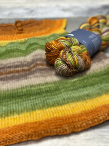 coloful striped child's handknit dress displayed with yarn